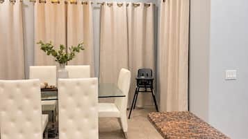 A dining area with a glass table, white upholstered chairs, a black folding chair, and a granite countertop.