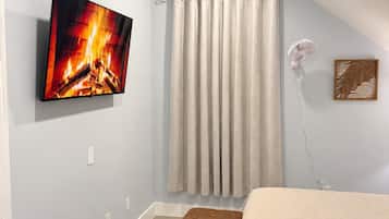 Une chambre à coucher avec un lit, un téléviseur fixé au mur, un ventilateur de plafond et une fenêtre avec des rideaux.