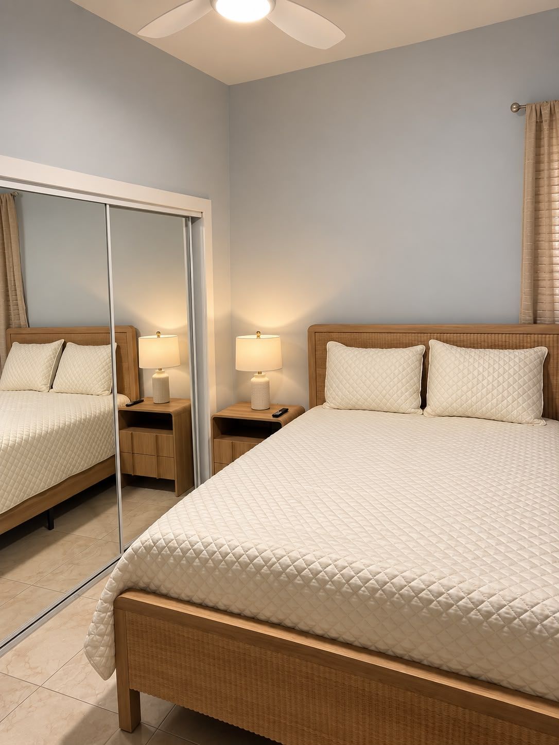 A hotel room with a large bed, a bedside table with a lamp, a mirror, and a ceiling fan.