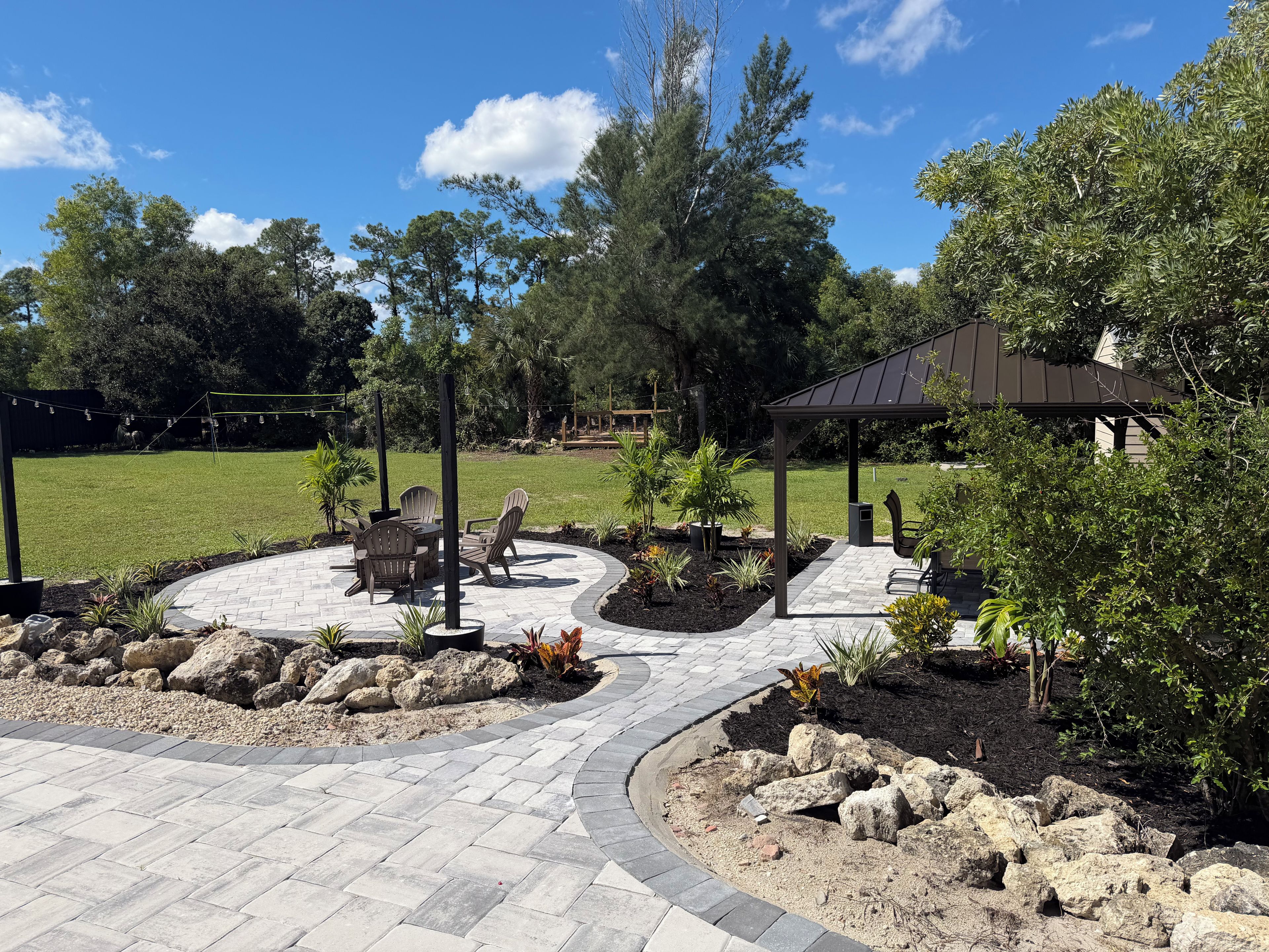 A patio area with a circular seating arrangement, a pergola, and a landscaped garden with rocks and plants.