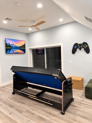 A pool table in a room with a ceiling fan, a mounted TV, and a wall-mounted game controller.
