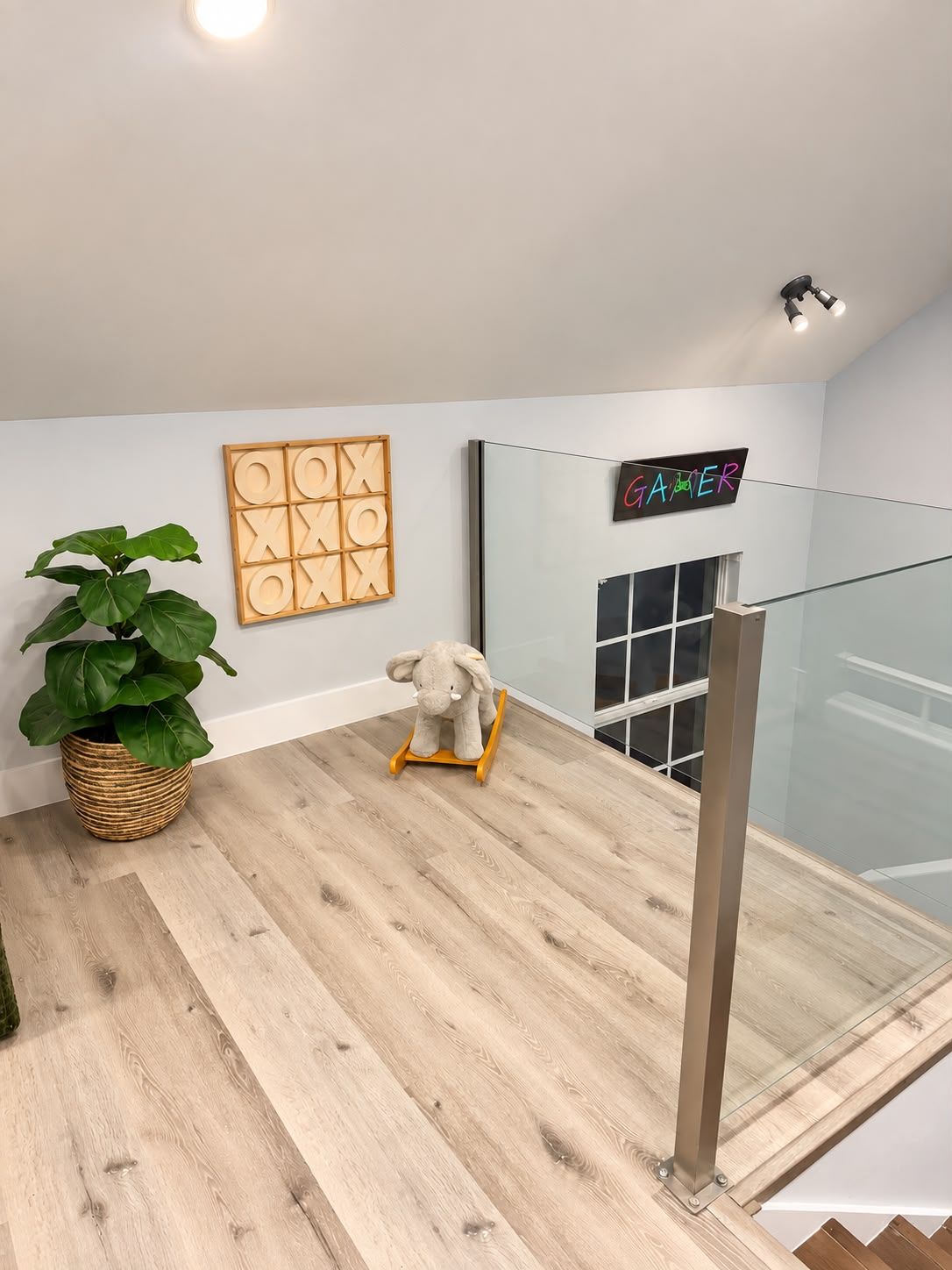 A modern interior with a wooden floor, a potted plant, a rocking elephant toy, a framed puzzle, and a neon sign.