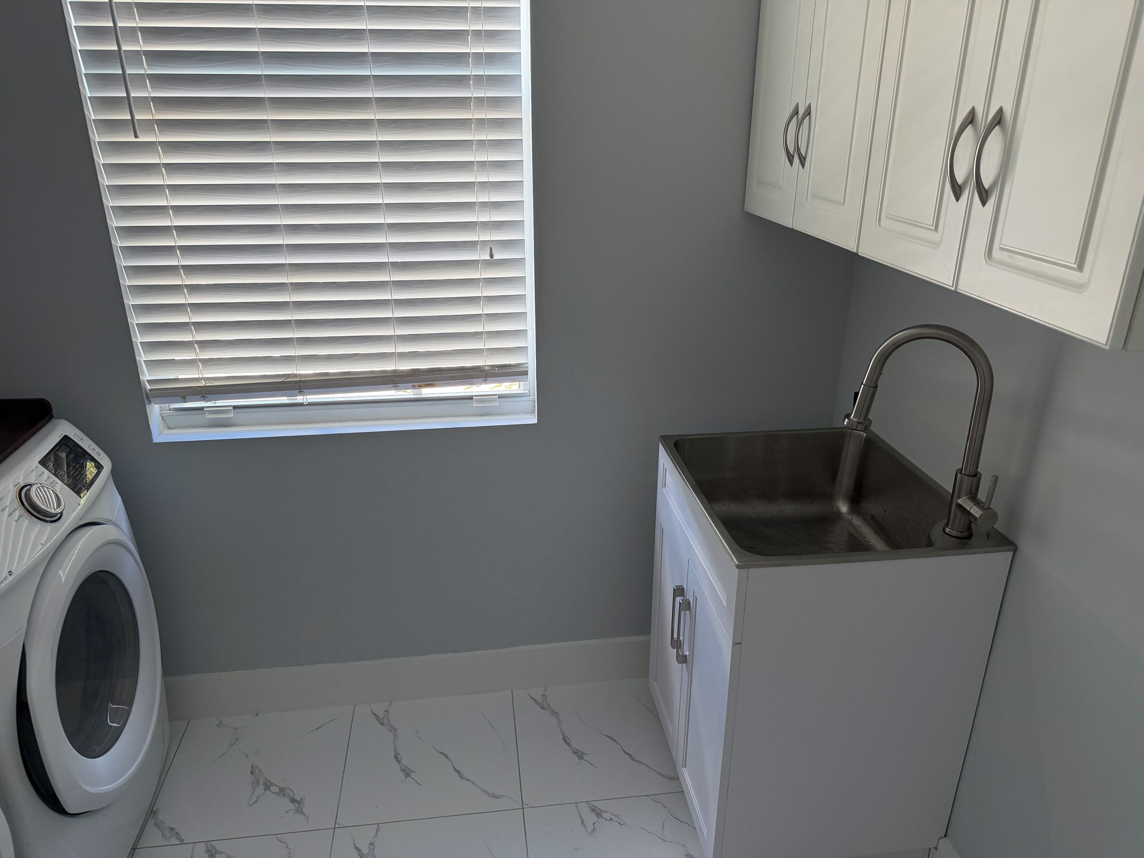 A laundry room with a washing machine, a sink, and a window with blinds.