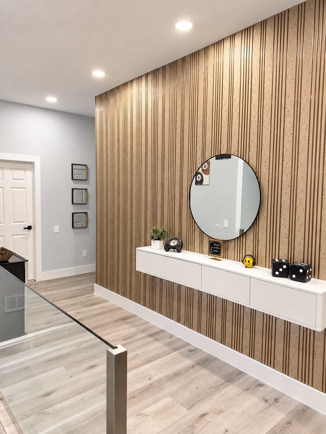 A modern bathroom with a wooden panel wall, a round mirror, a white vanity, and a glass shower enclosure.