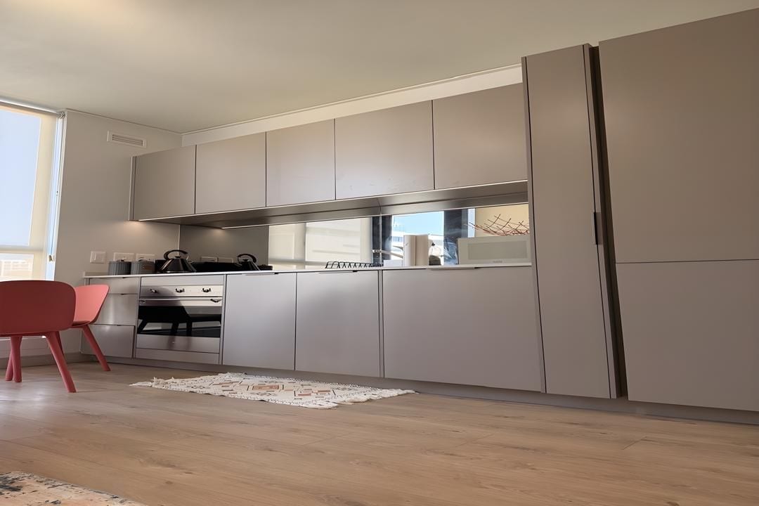 A modern kitchen with grey cabinets, a stainless steel oven, and a red chair.