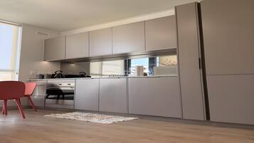 A modern kitchen with grey cabinets, a stainless steel oven, and a red chair.