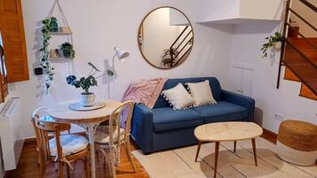 Salón con sofá azul, comedor redondo y escalera