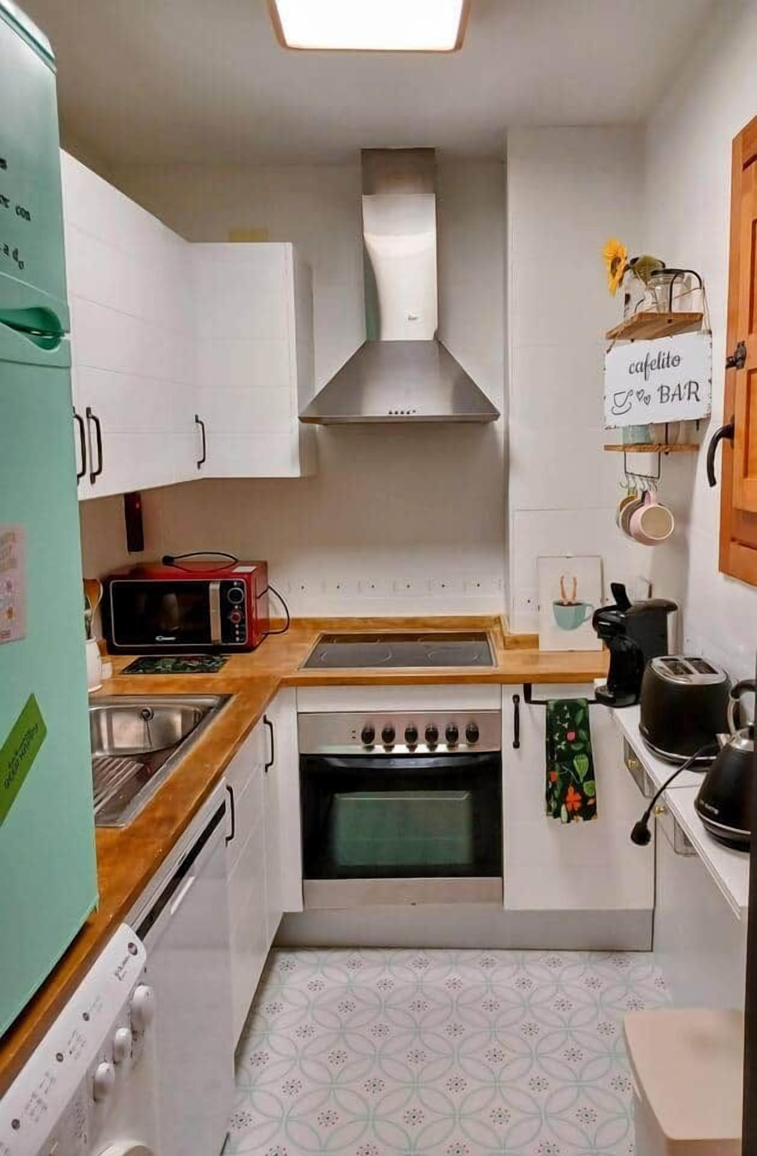 A compact kitchen with white cabinets, a microwave, a stove, and a sink.