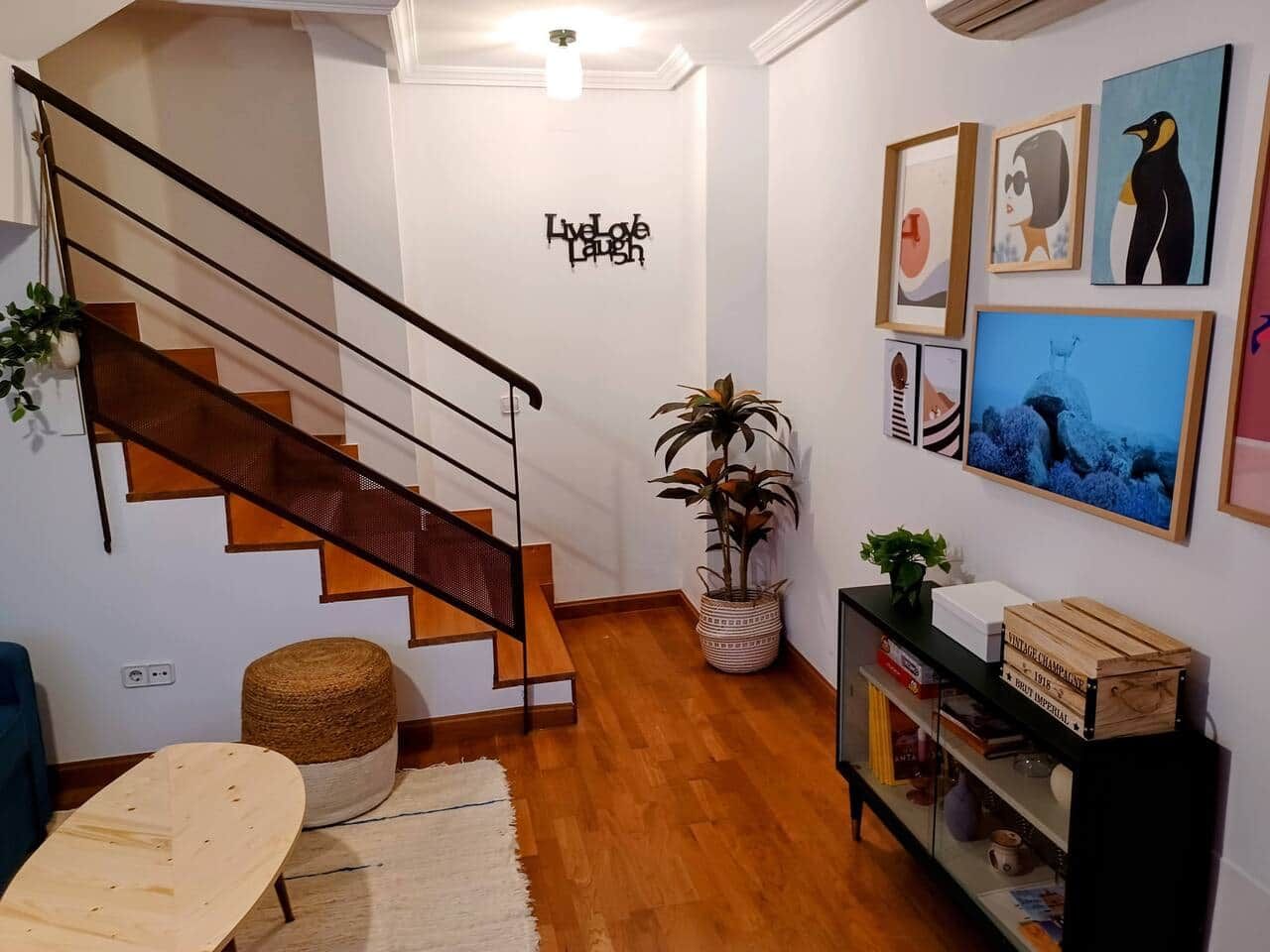 Een trap met een metalen leuning, een muur met een 'Live Love Laugh' bord, en een verzameling ingelijste kunstwerken aan de wand.