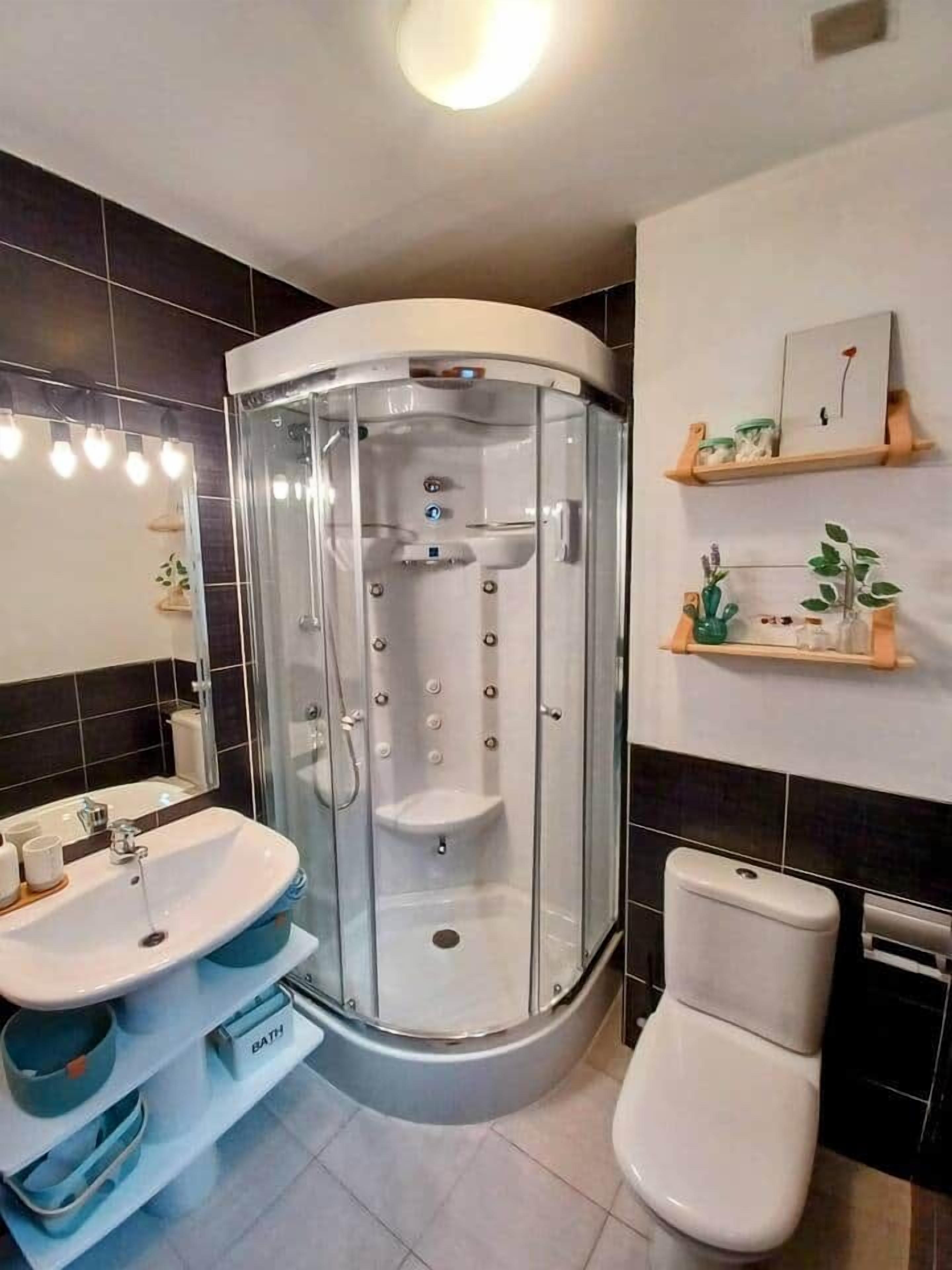 Een moderne badkamer met een glazen douchecabine, een witte wastafel en een toilet.