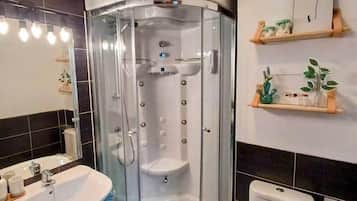 Een moderne badkamer met een glazen douchecabine, een witte wastafel en een toilet.