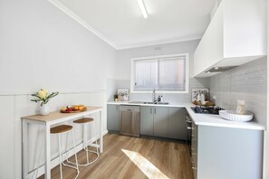 A modern kitchen with a central island, bar stools, a dishwasher, and a window with blinds. - Birch & Maple - Belmont (Belmont)
