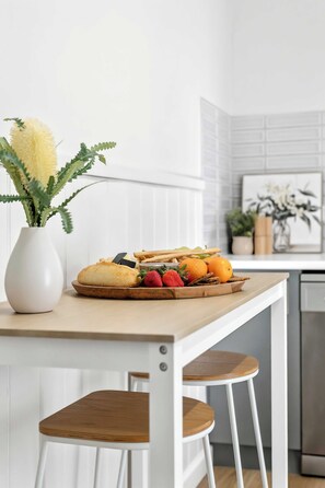 A kitchen with a white table, a vase with flowers, and a plate of food. - Birch & Maple - Belmont (Belmont)