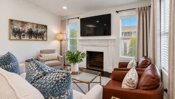 A living room with a fireplace, sofa, armchair, and a flat-screen TV mounted above it.
