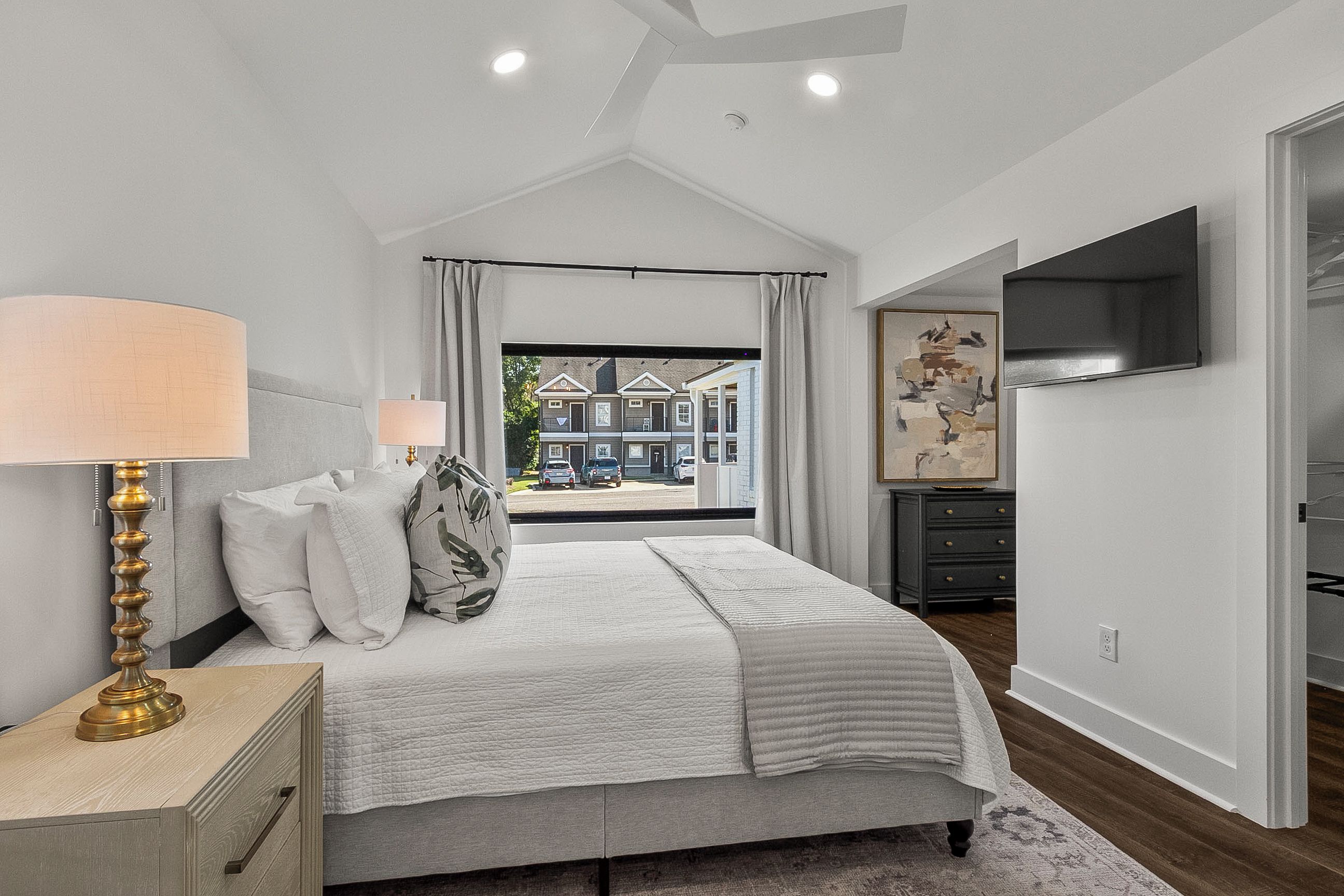 Een slaapkamer met een bed, nachtkastje, lamp en uitzicht op de straat.