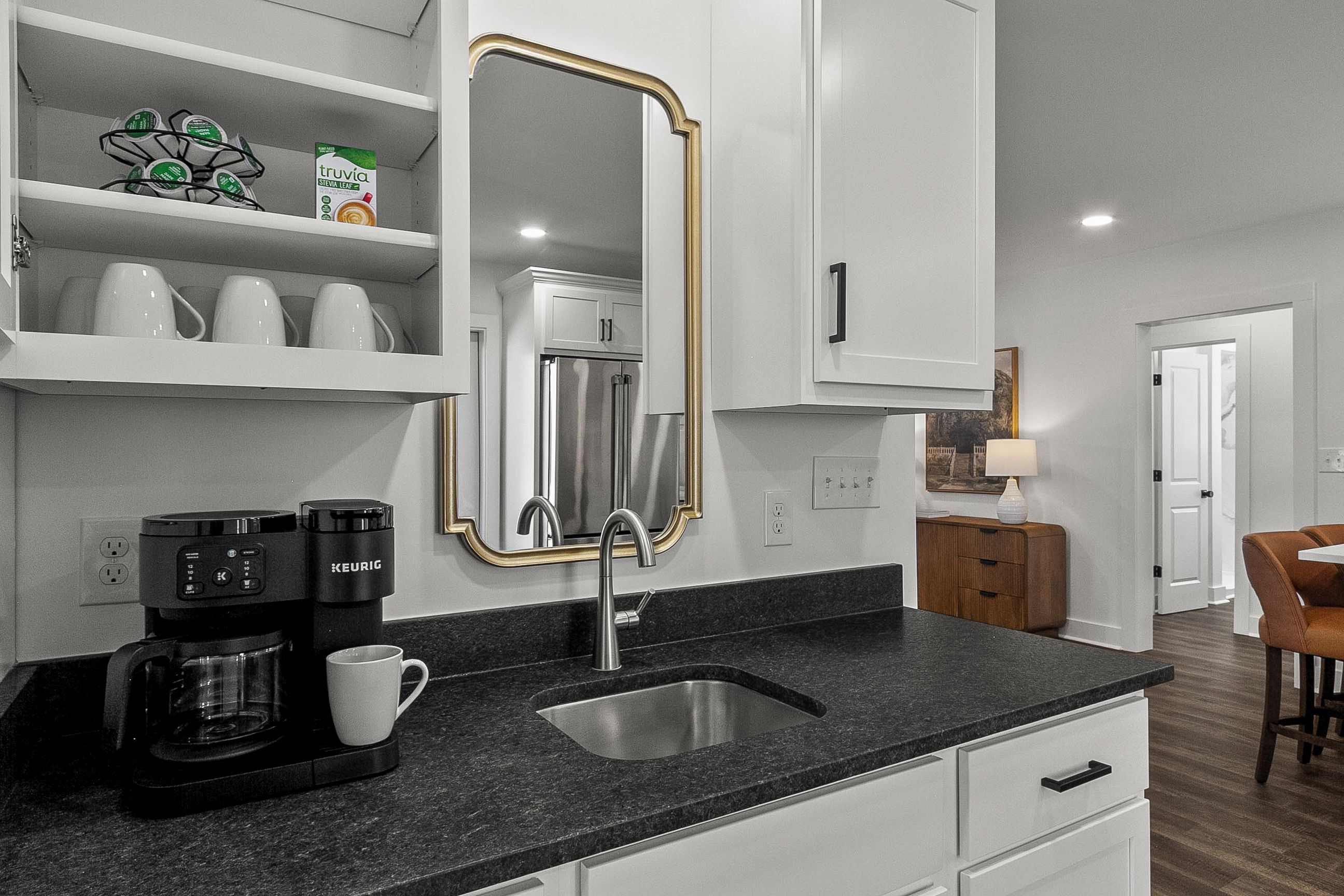 A kitchen with a black countertop, a coffee maker, a sink, and a refrigerator.