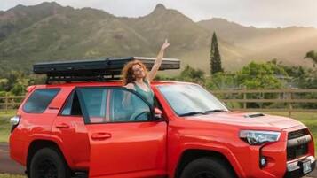 Un SUV rojo estacionado en un área con césped y montañas al fondo.