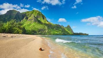 Uma praia com águas cristalinas, areal dourado e montanhas ao fundo.
