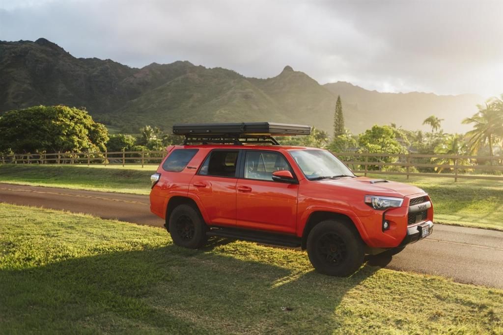 Un SUV rojo estacionado en un césped con montañas al fondo.