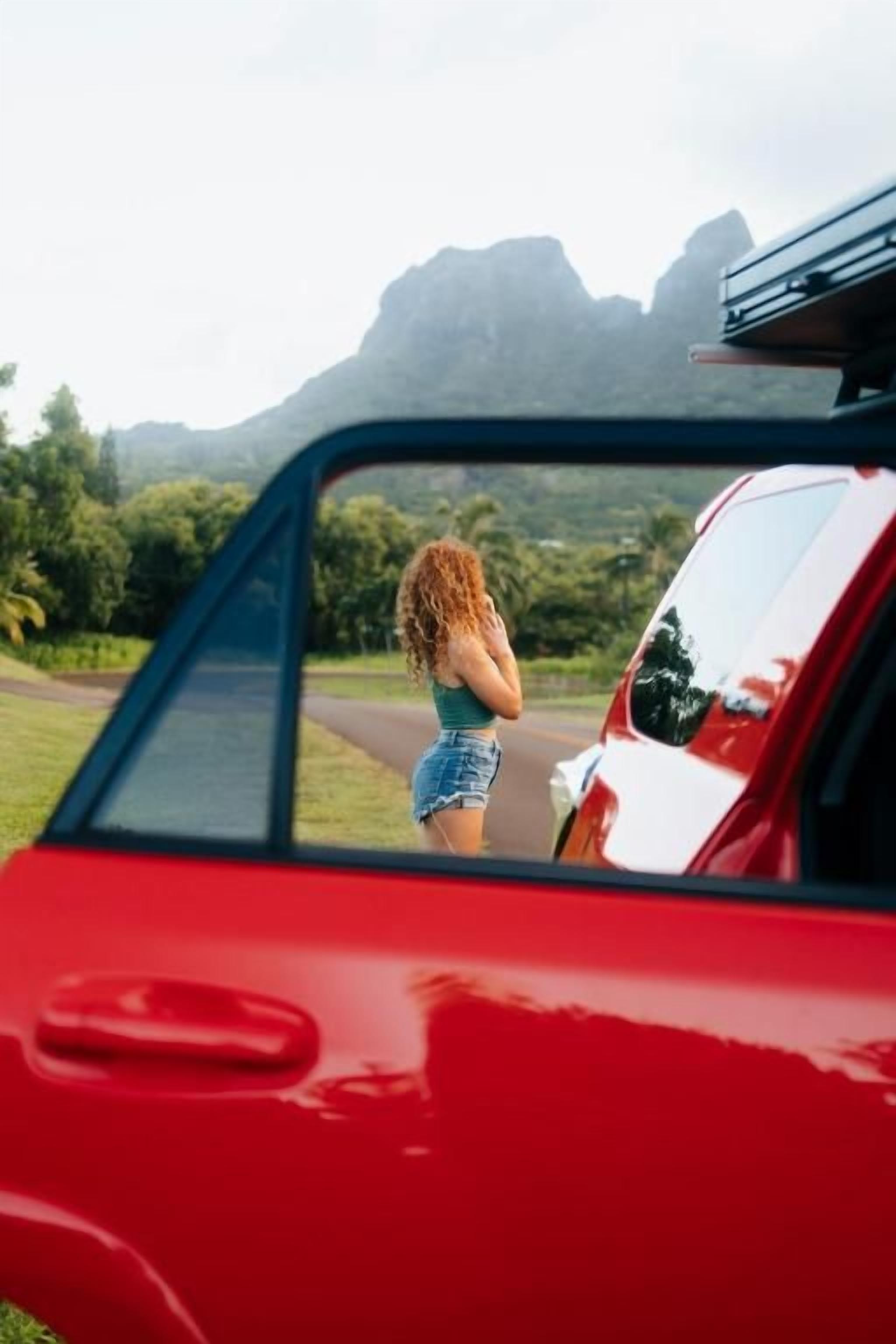 A red car with a rearview mirror reflecting a person standing outside.