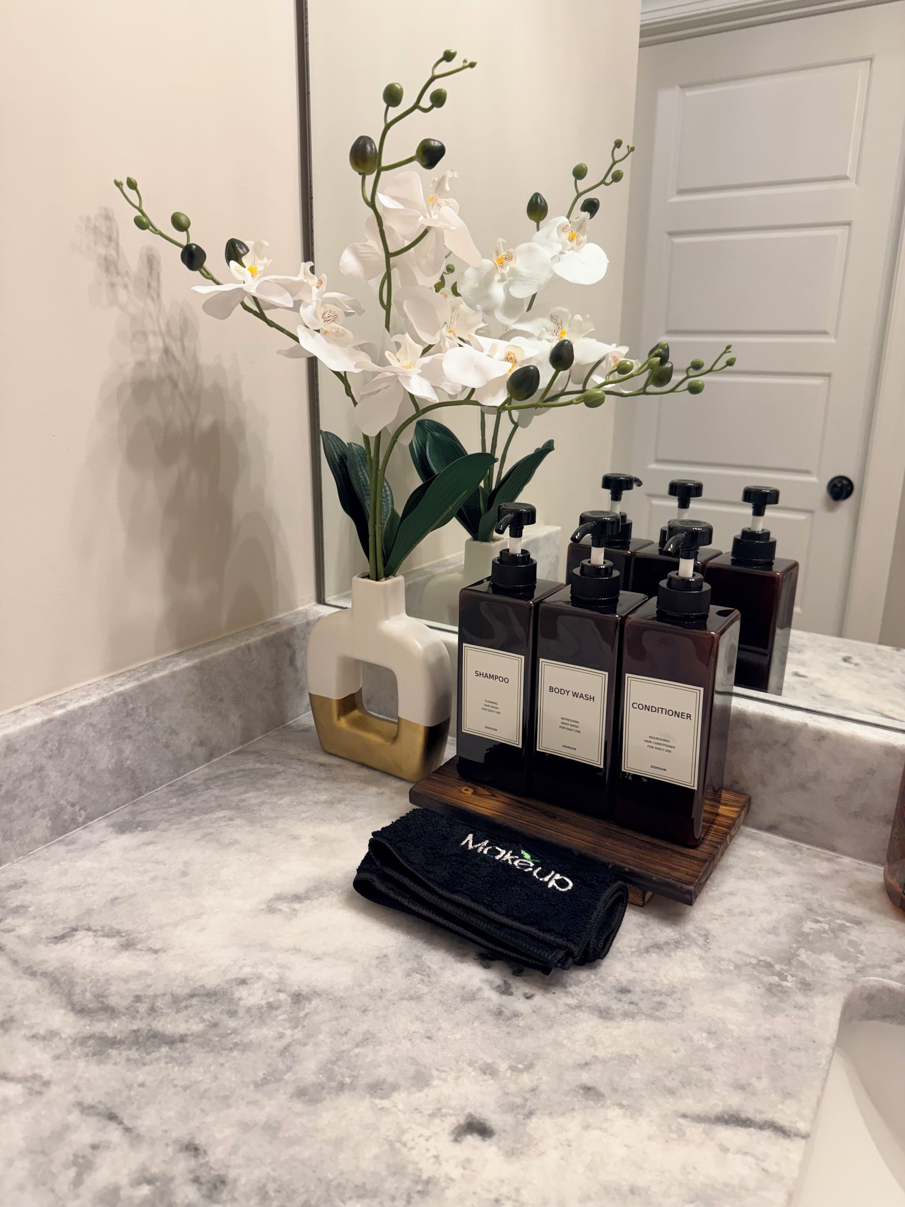 Ein Badezimmer-Waschtisch mit Marmorplatte, einer weißen Orchideenpflanze und einer Reihe von Pflegeprodukten, darunter Shampoo, Duschgel und Conditioner.