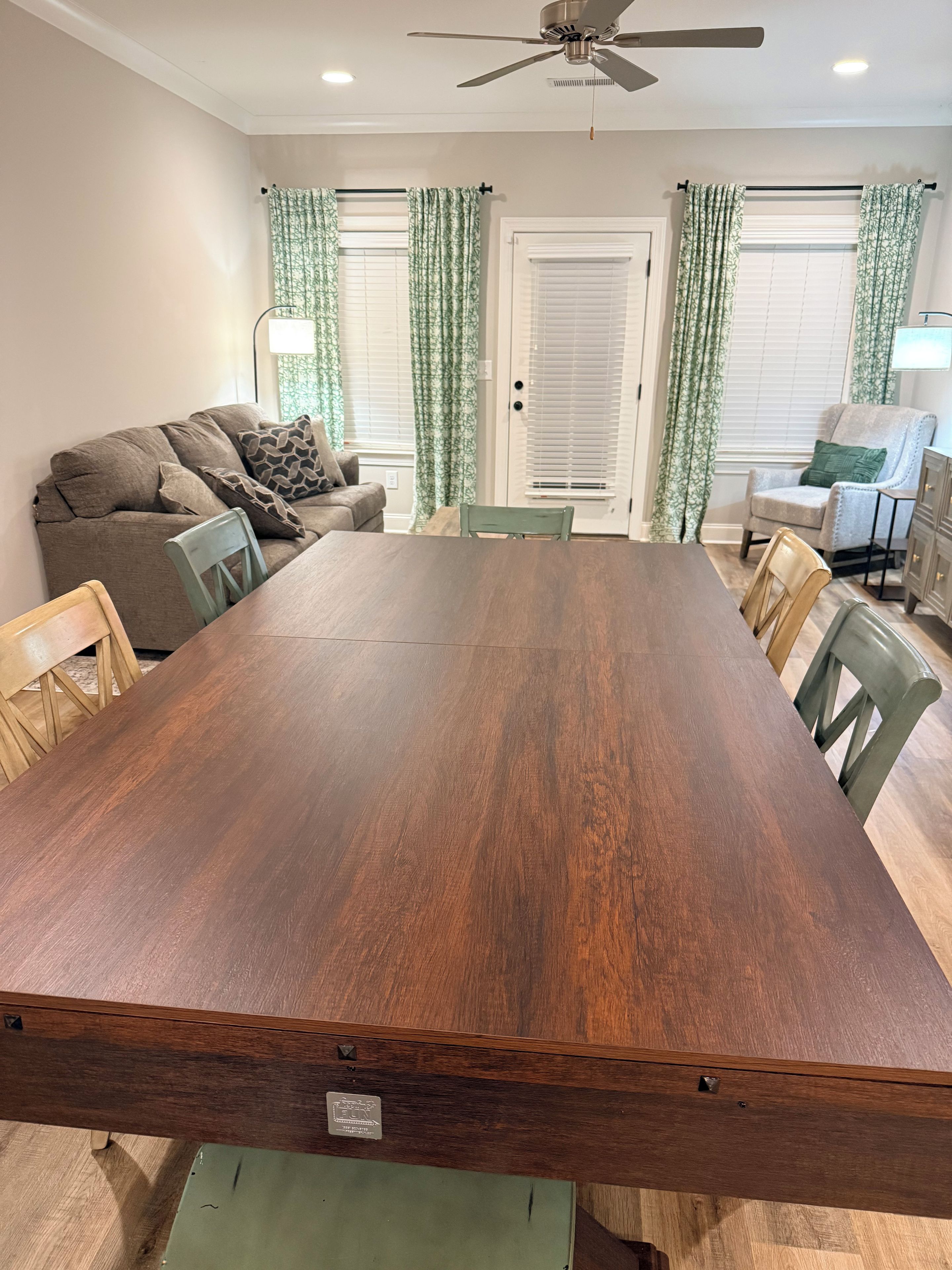 A dining area with a long wooden table, green chairs, a sofa, and a ceiling fan.