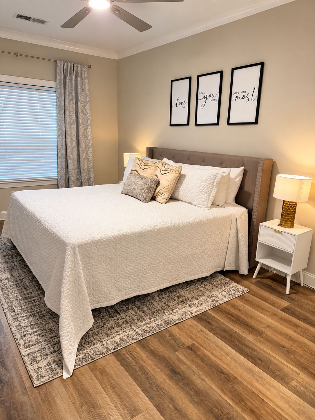 A bedroom with a bed, a nightstand, a ceiling fan, and three framed quotes on the wall.