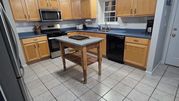 Una cucina con mobili in legno, un forno a microonde, un piano cottura, un lavello e un pavimento piastrellato.