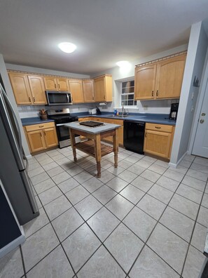 Una cocina con armarios de madera, microondas, estufa, pileta y piso con baldosas.