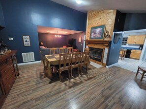 A dining area with a wooden table and chairs, a fireplace, and a kitchen in the background. - Quiet 3-Bedroom Country Stay in Nebo, Illinois (Nebo)
