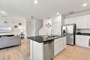 A modern kitchen with a central island, stainless steel appliances, and a dining area with a sofa and a TV. - Best location near Orlando’s world famous attractions (Kissimmee)