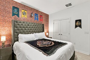 A bedroom with a brick wall, a tufted headboard, a white bedspread, and a Hogwarts-themed throw. - Best location near Orlando’s world famous attractions (Kissimmee)