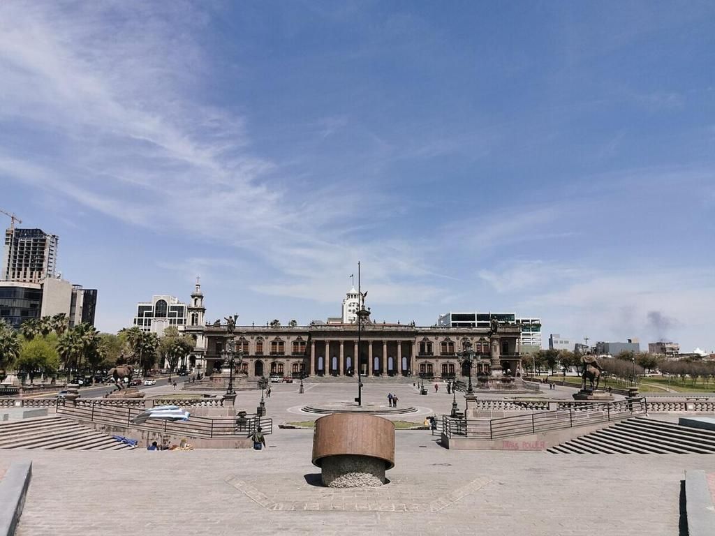 Una plaza con un edificio grande, escalones y un monumento central.