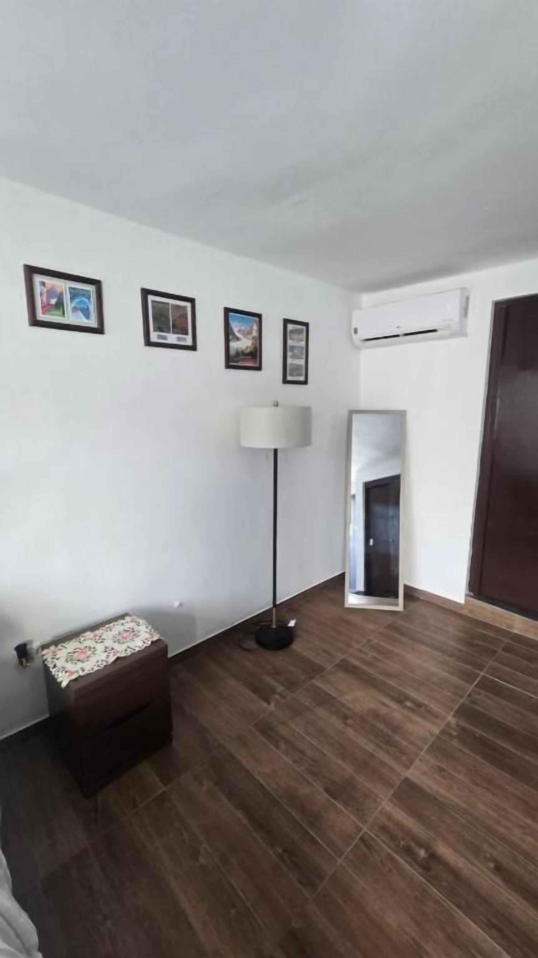 Um quarto com piso de madeira, luminária de chão, um pequeno banco e uma porta.