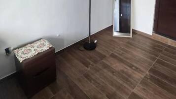 Um quarto com piso de madeira, luminária de chão, um pequeno banco e uma porta.