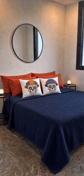Une chambre à coucher avec un lit, des oreillers, un miroir rond et une table de chevet.