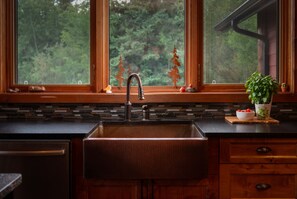 A kitchen with a large window, a sink, and a potted plant on the windowsill. - Luxury West Coast Post & Beam Estate on 142 Acres of Private Alberta Wilderness! (Westlock County)