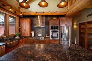 A kitchen with wooden cabinets, stainless steel appliances, and a granite countertop. - Luxury West Coast Post & Beam Estate on 142 Acres of Private Alberta Wilderness! (Westlock County)