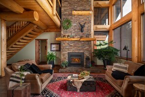 A spacious living room with a fireplace, wooden beams, and a high ceiling. - Luxury West Coast Post & Beam Estate on 142 Acres of Private Alberta Wilderness! (Westlock County)
