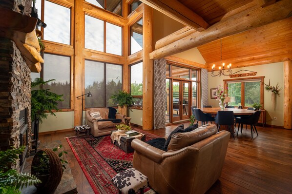 A spacious log cabin interior with a large dining area, multiple seating options, and a fireplace. - Luxury West Coast Post & Beam Estate on 142 Acres of Private Alberta Wilderness! (Westlock County)