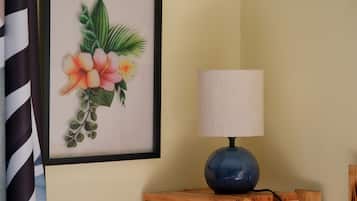 Un'opera d'arte floreale incorniciata su una parete, una lampada blu su un tavolo in legno e una tenda a righe parzialmente visibile.