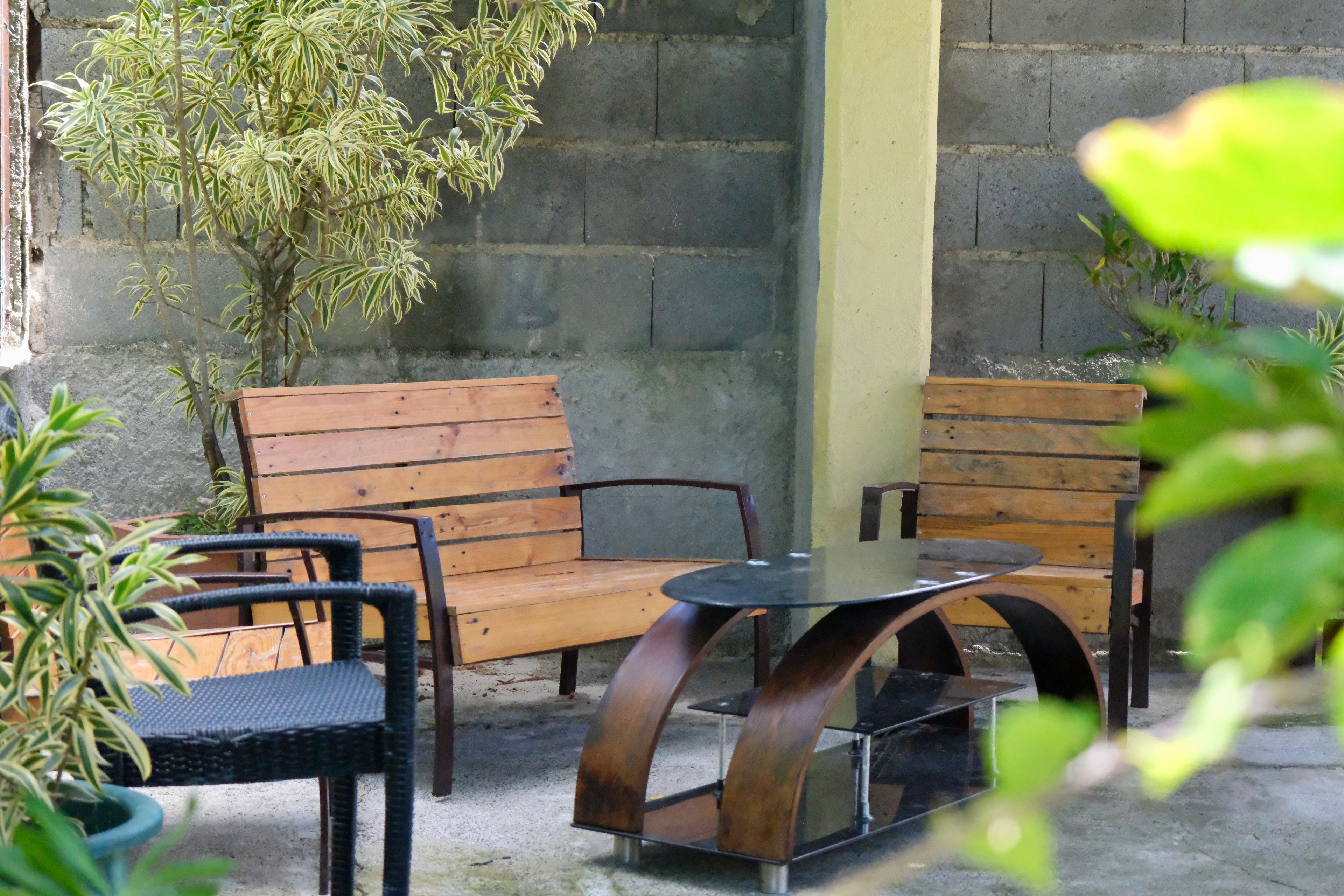 A seating area with wooden benches and a glass table, surrounded by plants.