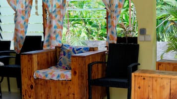 A wooden outdoor seating area with a chair and a table, surrounded by a yellow wall and green plants.