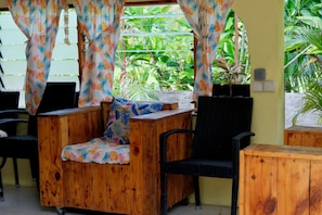 A wooden outdoor seating area with a chair and a table, surrounded by a yellow wall and green plants. - Povai lodge (Bora-Bora)