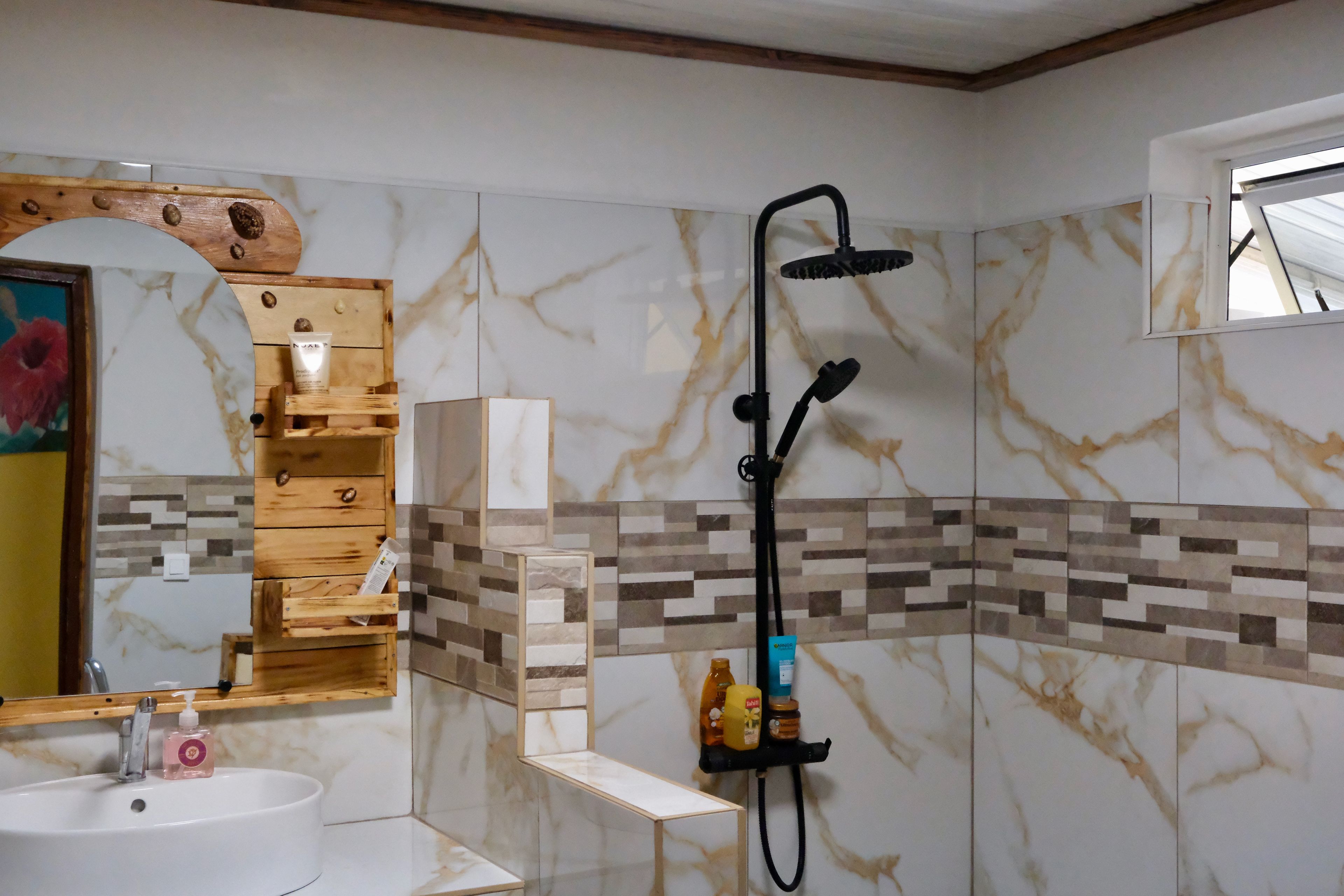 A bathroom with a marble wall, a wooden vanity, a sink, and a shower.