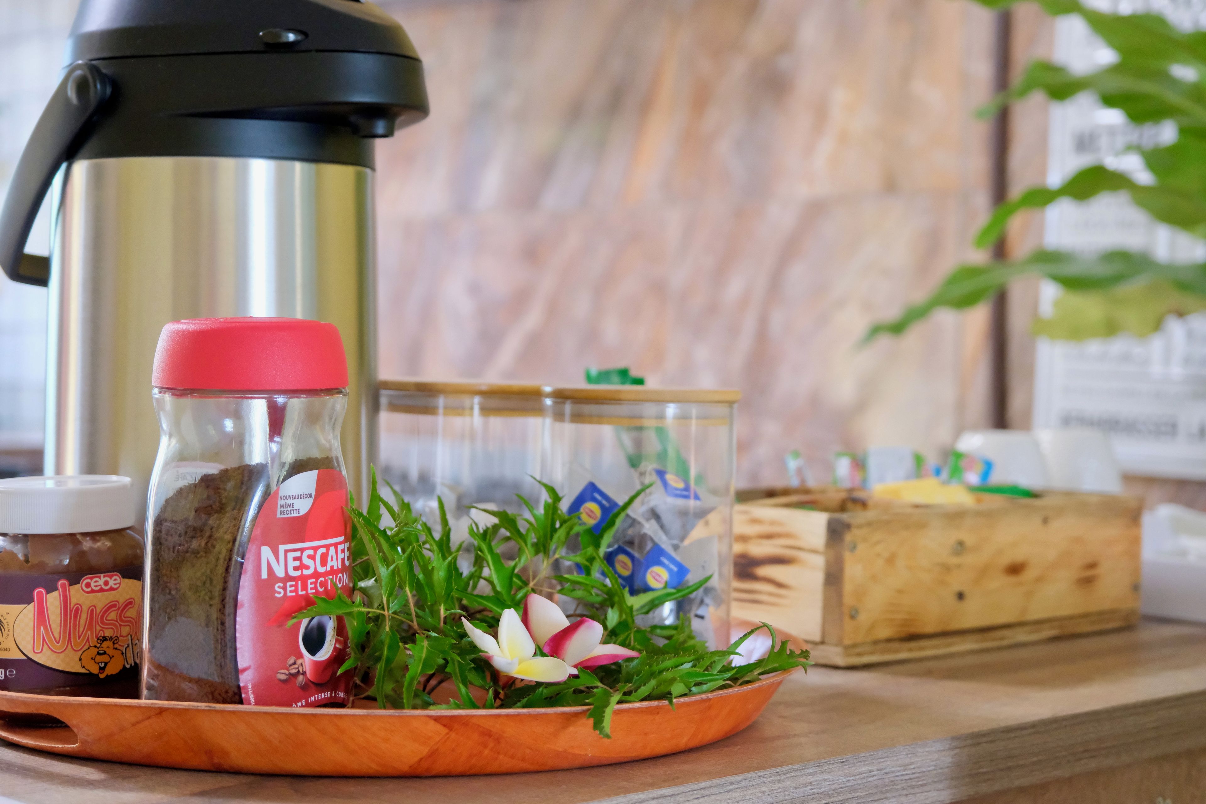 Un comptoir de cuisine avec une machine à café, un bocal de café Nescafé, un pot de beurre de cacahuète, un bol de feuilles vertes et une boîte en bois.