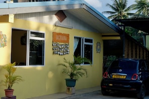 A yellow building with a sign reading 'IAORANA,' a parked car, and potted plants. - Povai lodge (Bora-Bora)