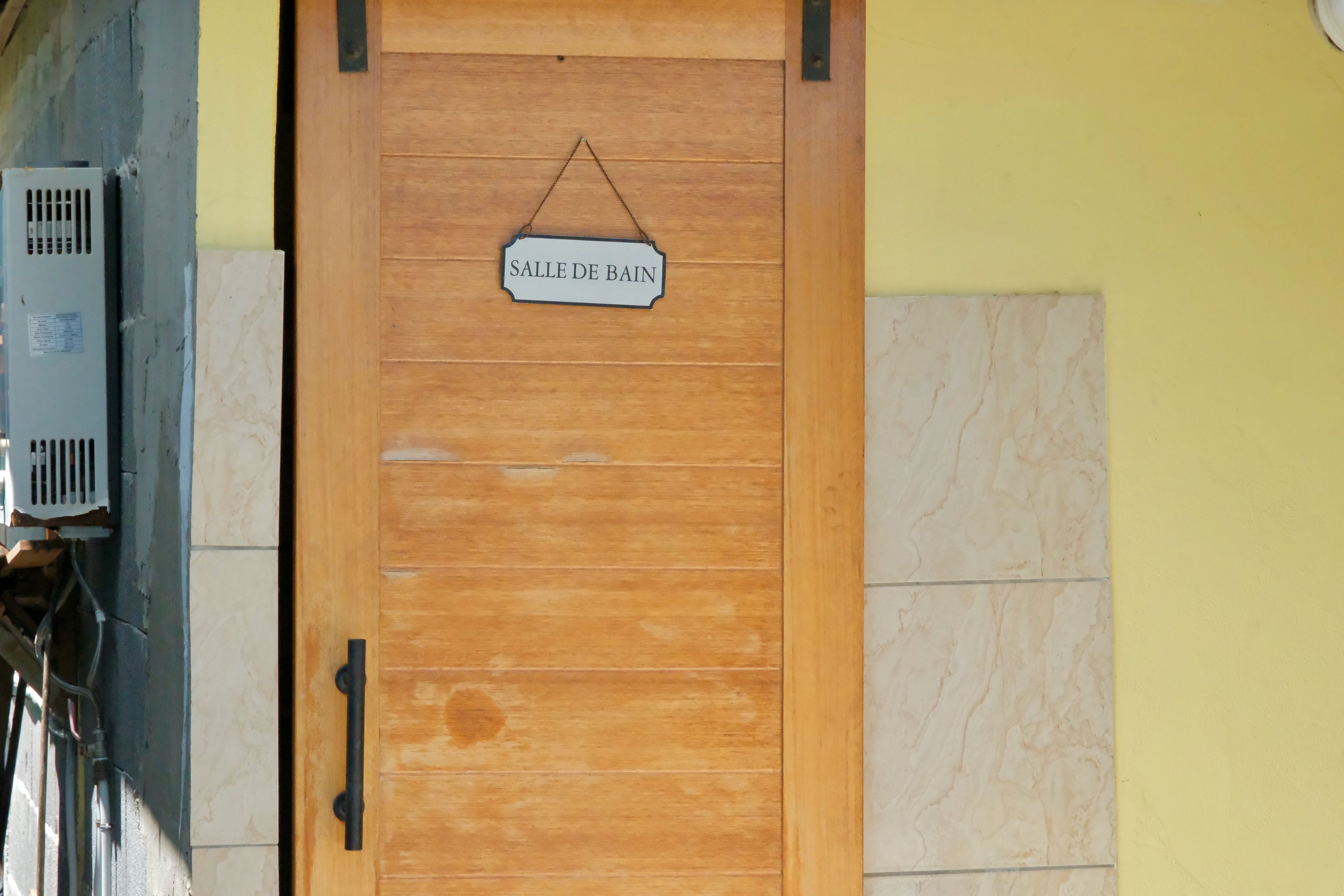 A wooden door with a sign reading 'SALLE DE BAIN' and a metal vent on the left.