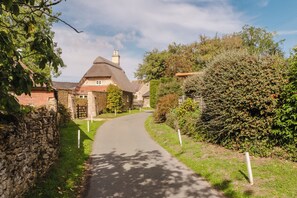 A narrow paved path leading to a stone building with a thatched roof, surrounded by greenery and stone walls. - Hoglets - Cosy Countryside Retreat (Conderton)
