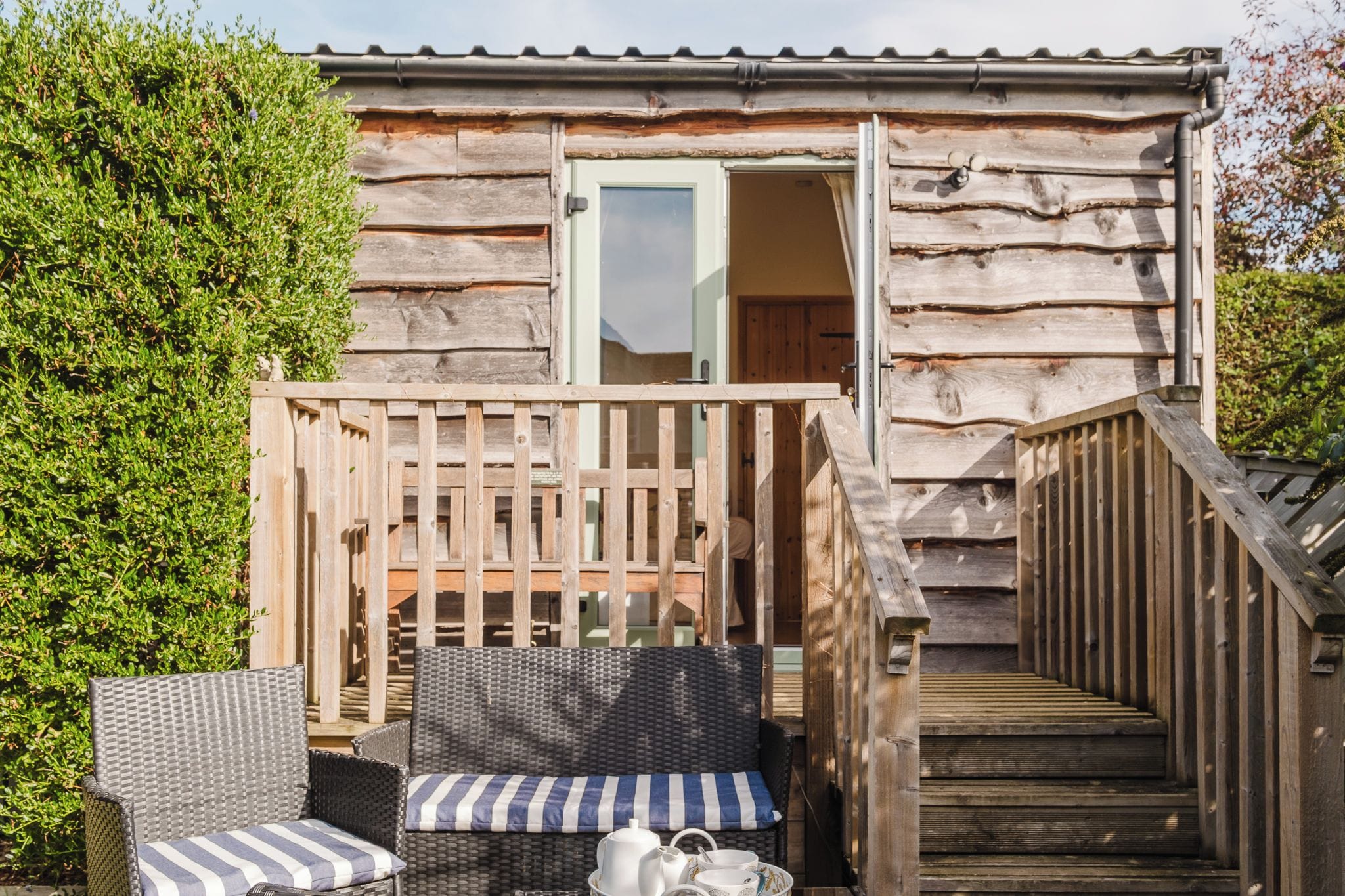 A wooden cabin with a balcony, outdoor seating, and a staircase leading to the entrance.